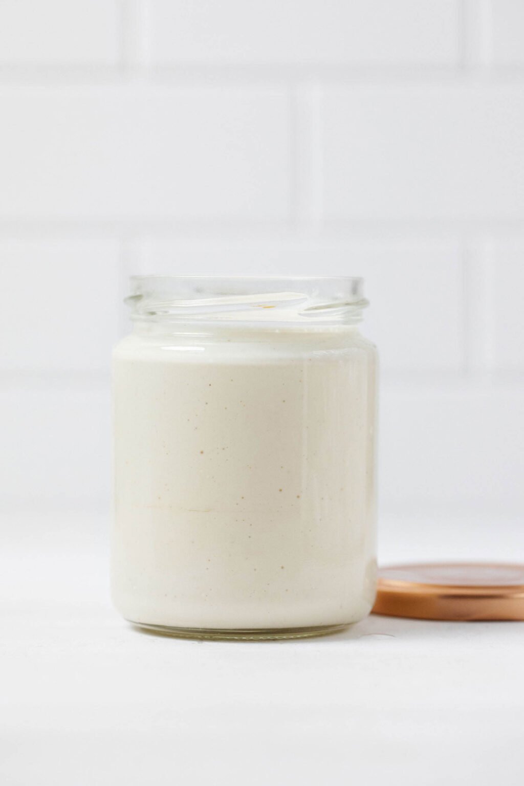 A mason jar has been filled with a vegan mayo, made from cashews. It rests on a white surface.