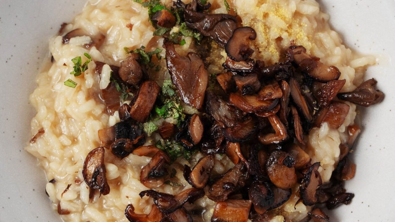 An overhead image of vegan mushroom risotto, which is garnished with green herbs and served in a white bowl.